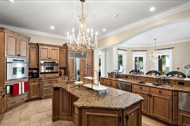 kitchen featuring a large island with sink, sink, ornamental molding, hanging light fixtures, and appliances with stainless steel finishes