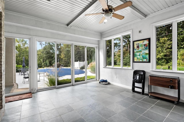 unfurnished sunroom featuring ceiling fan, beam ceiling, wooden ceiling, and a healthy amount of sunlight