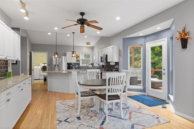 dining room with ceiling fan, washing machine and clothes dryer, vaulted ceiling, and light hardwood / wood-style floors