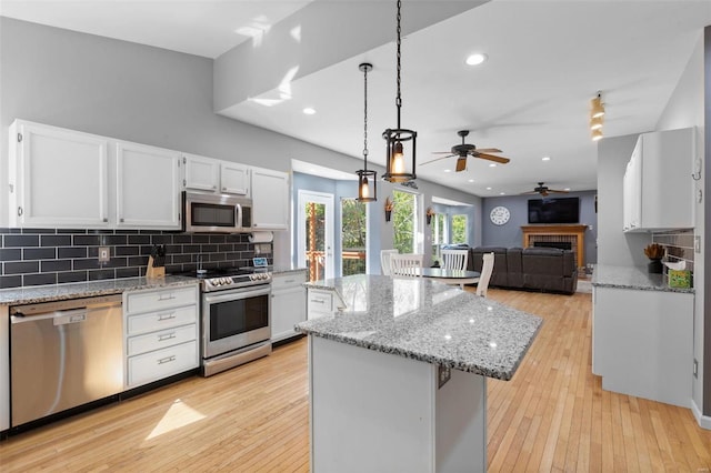 kitchen featuring light wood-type flooring, a center island, hanging light fixtures, white cabinetry, and appliances with stainless steel finishes