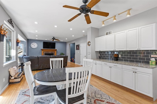 dining area featuring ceiling fan, light wood-type flooring, and a tiled fireplace