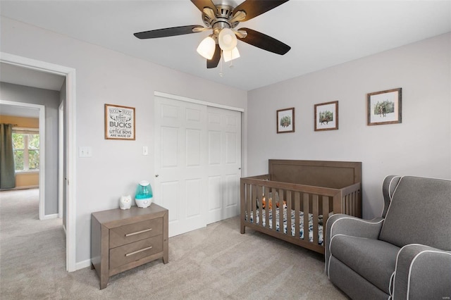 bedroom with a crib, a closet, light carpet, and ceiling fan