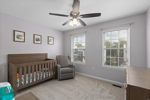 carpeted bedroom featuring a crib and ceiling fan