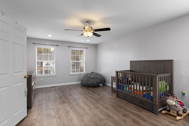 bedroom with a crib, light hardwood / wood-style floors, and ceiling fan