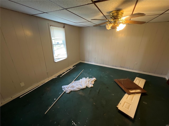 spare room featuring ceiling fan, wooden walls, and a drop ceiling