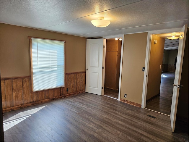 empty room with a textured ceiling, wood walls, and dark wood-type flooring