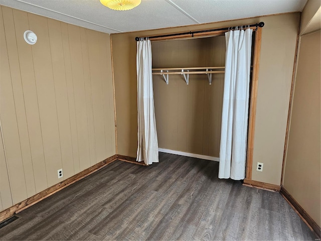 unfurnished bedroom with wood walls, dark wood-type flooring, and a closet