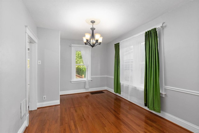 empty room with wood-type flooring and an inviting chandelier