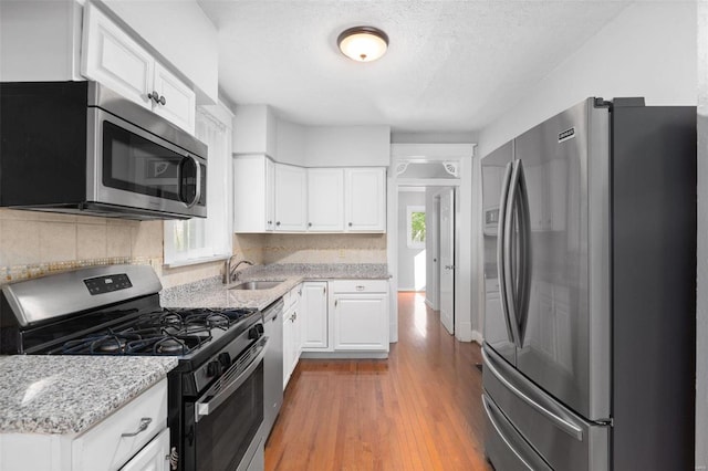 kitchen with light hardwood / wood-style flooring, sink, stainless steel appliances, backsplash, and white cabinets