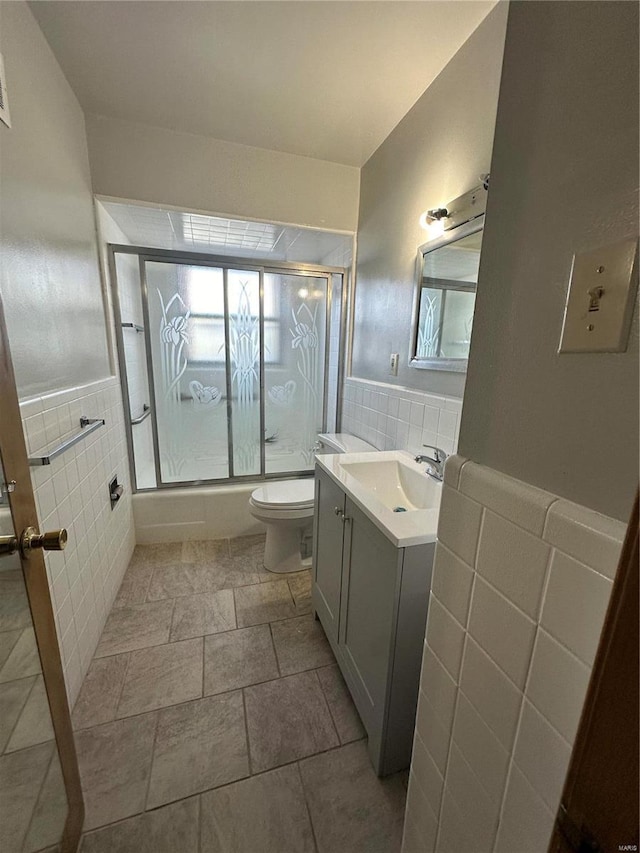 full bathroom with tile walls, vanity, toilet, and combined bath / shower with glass door