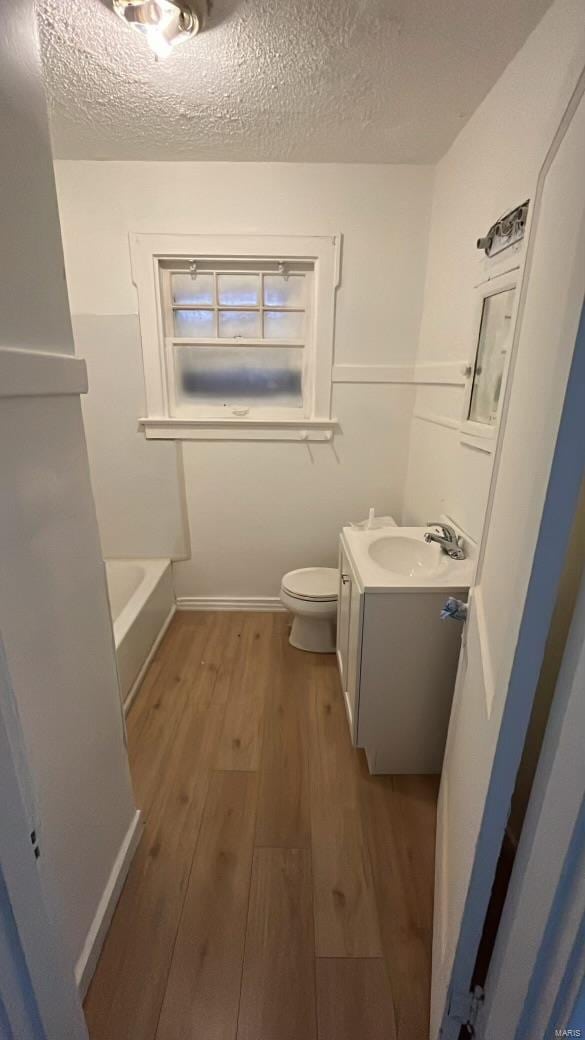 bathroom with vanity, a textured ceiling, hardwood / wood-style flooring, a tub to relax in, and toilet