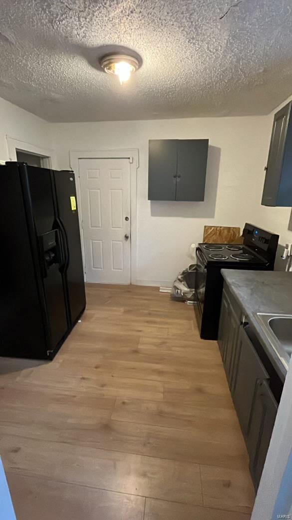 kitchen with light hardwood / wood-style flooring, black appliances, and a textured ceiling