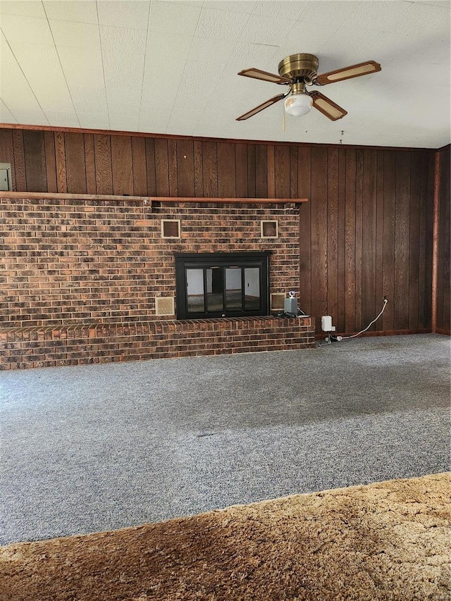 unfurnished living room featuring carpet flooring, ceiling fan, a fireplace, wood walls, and a textured ceiling