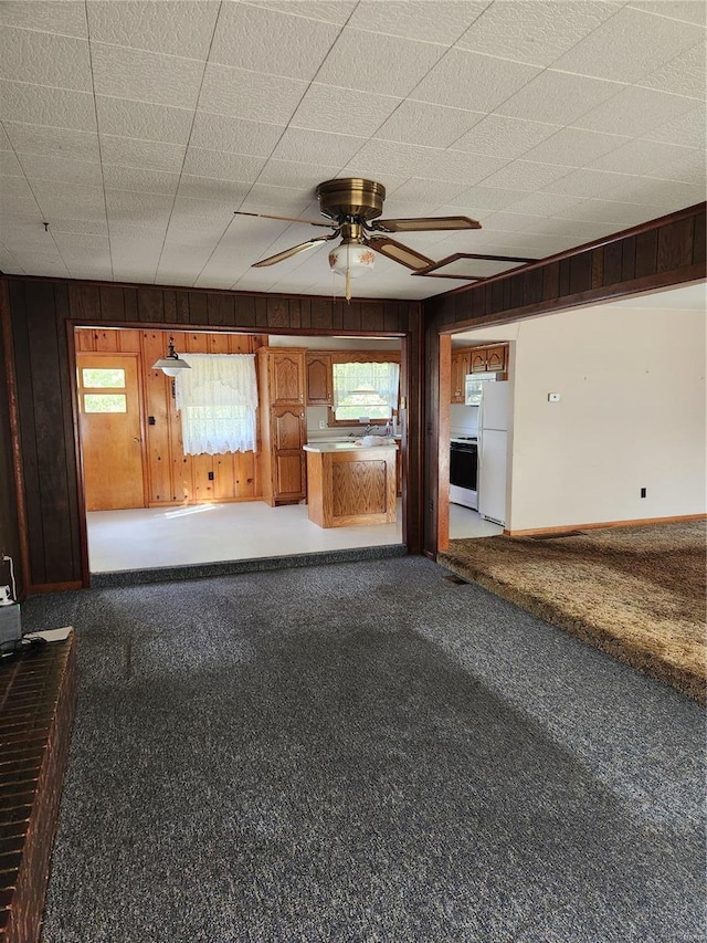 unfurnished living room with wood walls, carpet floors, sink, and ceiling fan