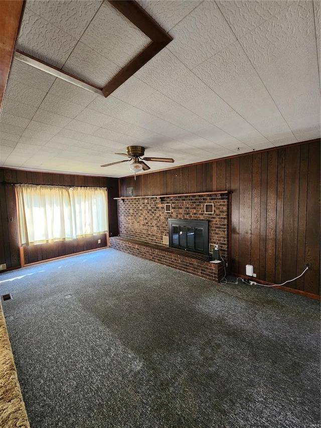 unfurnished living room with carpet floors, a fireplace, wood walls, and ceiling fan