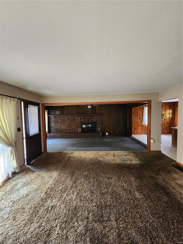 unfurnished living room featuring a fireplace, dark colored carpet, and wooden walls