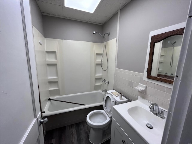 full bathroom featuring a drop ceiling, vanity,  shower combination, tile walls, and toilet