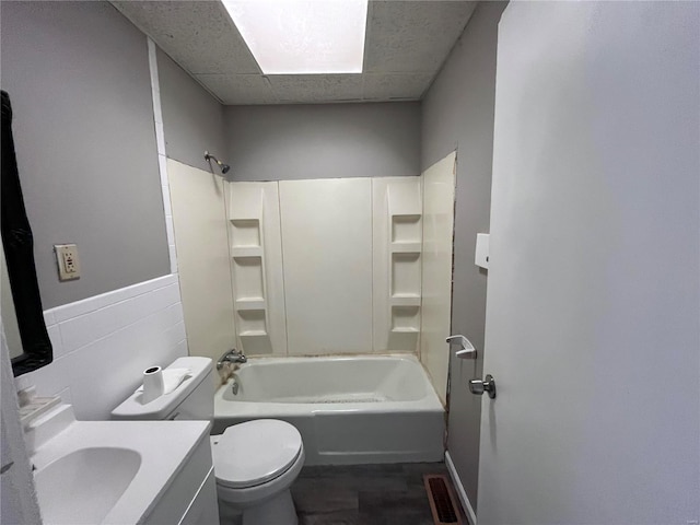 full bathroom with washtub / shower combination, toilet, a paneled ceiling, vanity, and tile walls