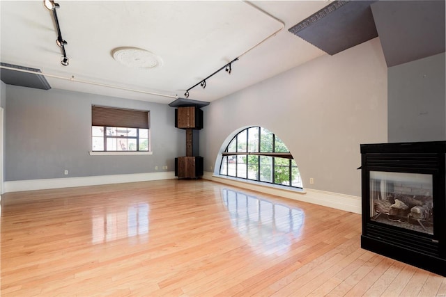 unfurnished living room with light wood-style flooring, baseboards, track lighting, and a multi sided fireplace