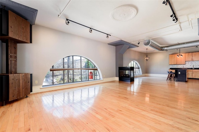 unfurnished living room featuring baseboards, rail lighting, a sink, and light wood-style floors