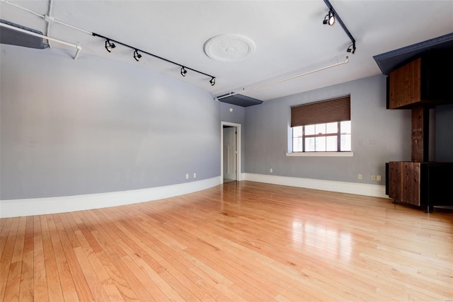 empty room featuring light wood-type flooring, track lighting, and baseboards