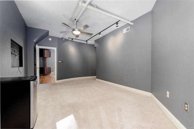 empty room with light colored carpet, visible vents, a ceiling fan, baseboards, and track lighting