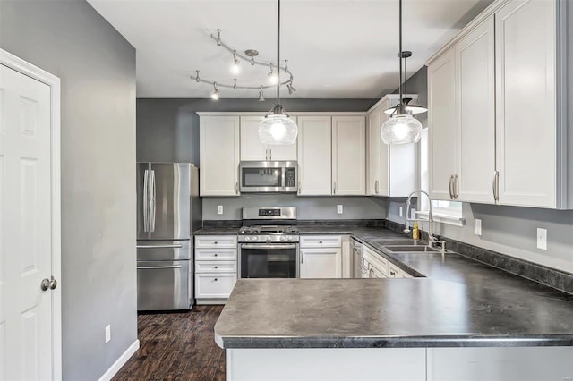 kitchen with kitchen peninsula, hanging light fixtures, appliances with stainless steel finishes, white cabinetry, and sink