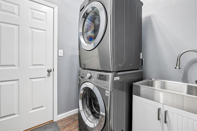 laundry room featuring dark wood-type flooring, stacked washer / drying machine, cabinets, and sink