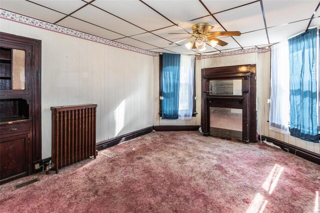 carpeted empty room with radiator heating unit, a paneled ceiling, and ceiling fan