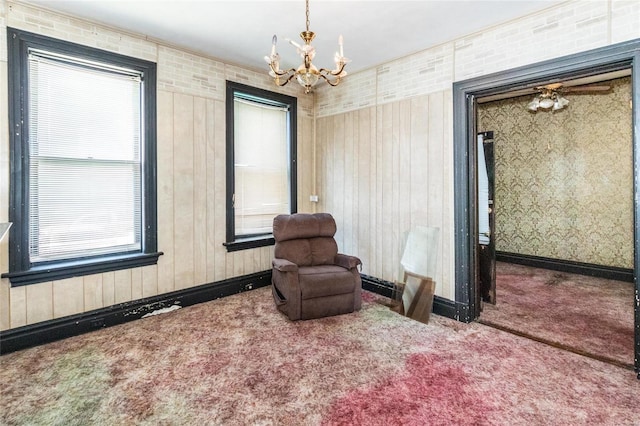 sitting room featuring wooden walls, carpet flooring, a wealth of natural light, and a chandelier