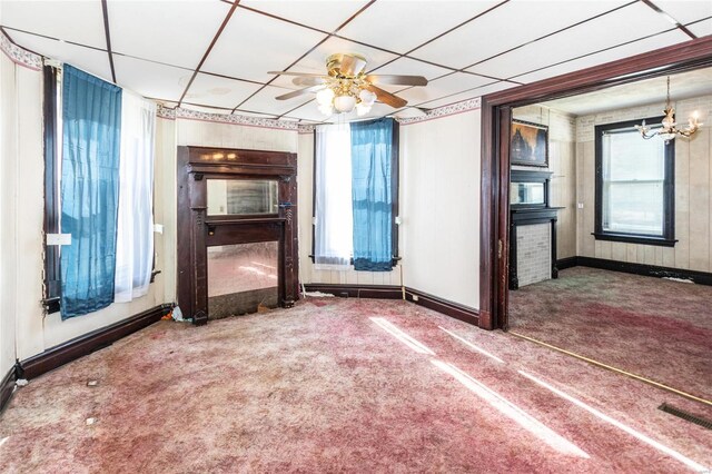 unfurnished living room with a drop ceiling, carpet flooring, and ceiling fan with notable chandelier