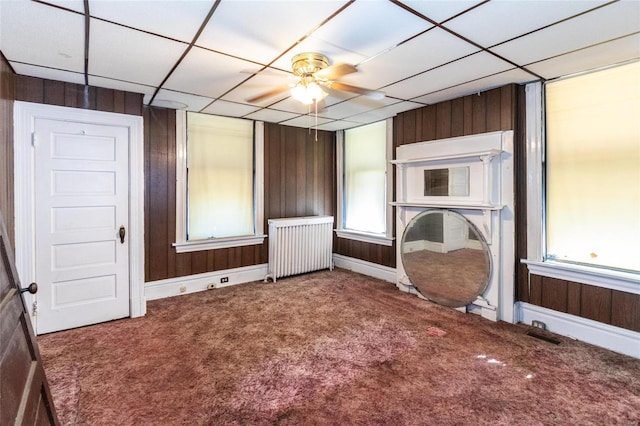 interior space featuring radiator, a drop ceiling, and wooden walls