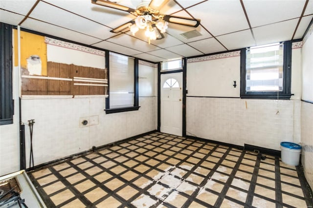 interior space featuring a paneled ceiling, tile walls, and ceiling fan