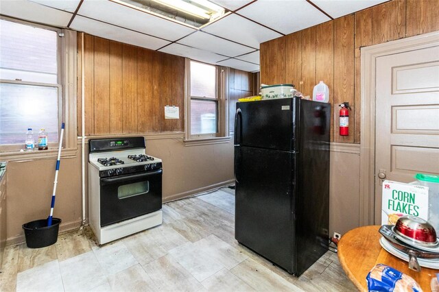 kitchen featuring a drop ceiling, wood walls, white gas range oven, and black fridge