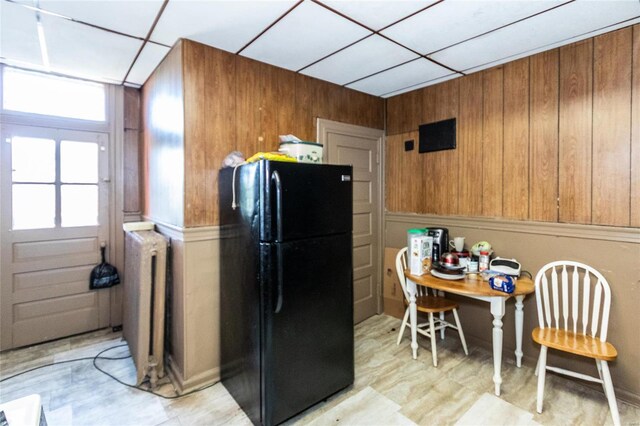 kitchen with wood walls, radiator, a paneled ceiling, and black fridge