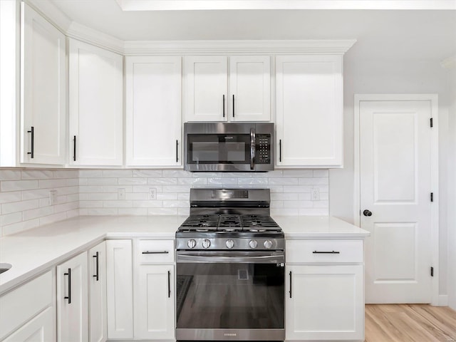 kitchen with tasteful backsplash, light hardwood / wood-style flooring, white cabinets, and appliances with stainless steel finishes