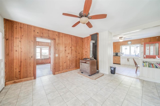 unfurnished living room featuring ceiling fan, wood walls, a wood stove, and a healthy amount of sunlight