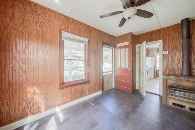 spare room featuring ceiling fan, wooden walls, and a wood stove