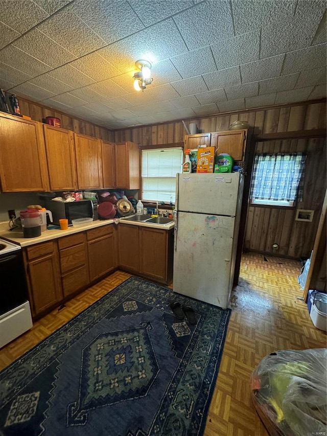 kitchen with wooden walls, white appliances, parquet floors, and sink