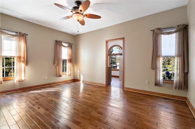 unfurnished room featuring ceiling fan, a healthy amount of sunlight, and dark hardwood / wood-style flooring