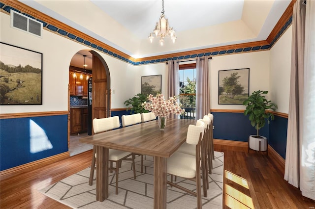 dining area with a notable chandelier, a tray ceiling, and wood-type flooring