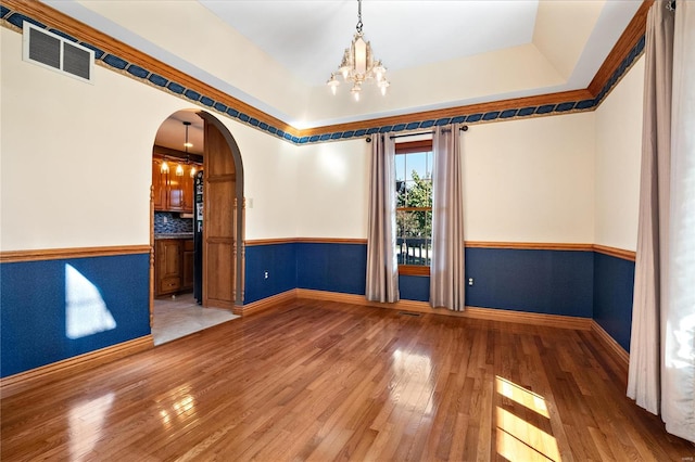 spare room featuring hardwood / wood-style flooring, a chandelier, and a tray ceiling