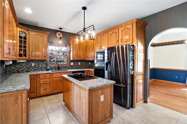 kitchen featuring pendant lighting, sink, light stone counters, black appliances, and a kitchen island