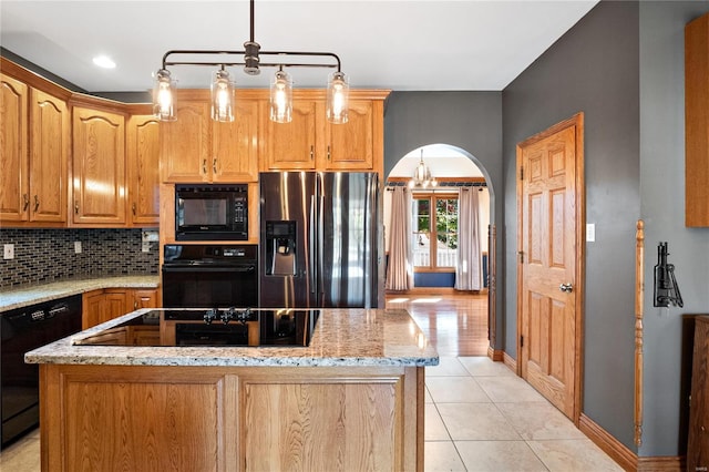 kitchen with backsplash, hanging light fixtures, a center island, light stone counters, and black appliances