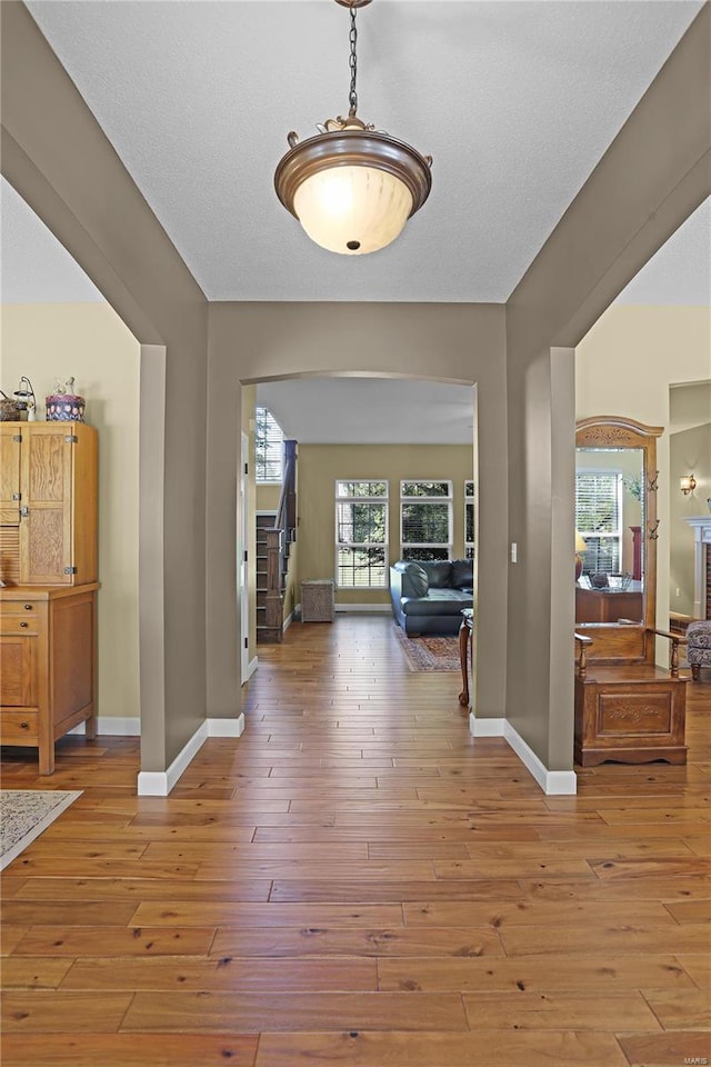 hall with a wealth of natural light, a textured ceiling, and hardwood / wood-style floors