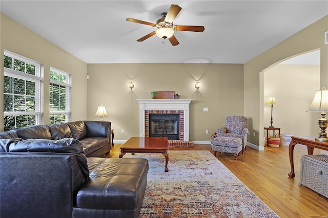 living room with a brick fireplace, hardwood / wood-style flooring, and ceiling fan