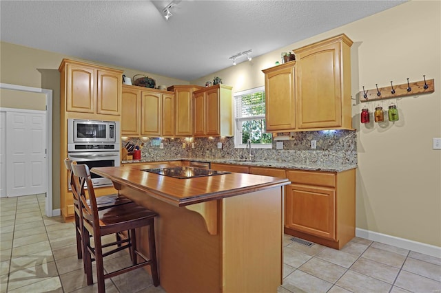 kitchen featuring decorative backsplash, appliances with stainless steel finishes, track lighting, and light tile patterned floors