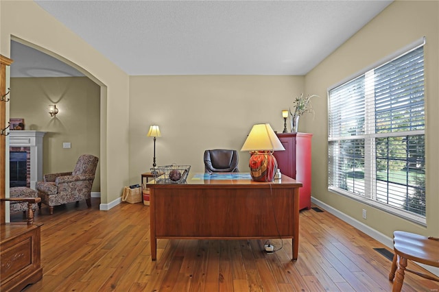 office featuring a brick fireplace, hardwood / wood-style flooring, a textured ceiling, and a healthy amount of sunlight