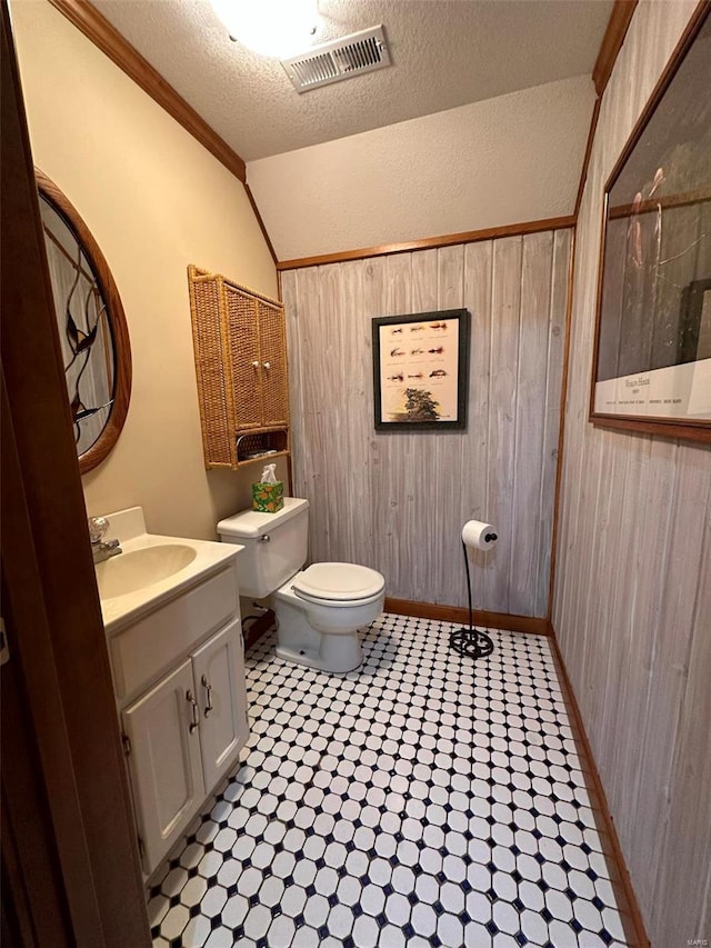 bathroom with wooden walls, toilet, vanity, and vaulted ceiling