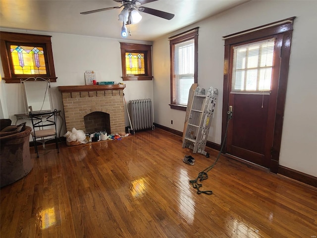 living room with hardwood / wood-style flooring, ceiling fan, radiator heating unit, and a brick fireplace